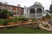 Garden courtyard with a white gazebo, stone-edged planting beds and a red-brick building in the background.