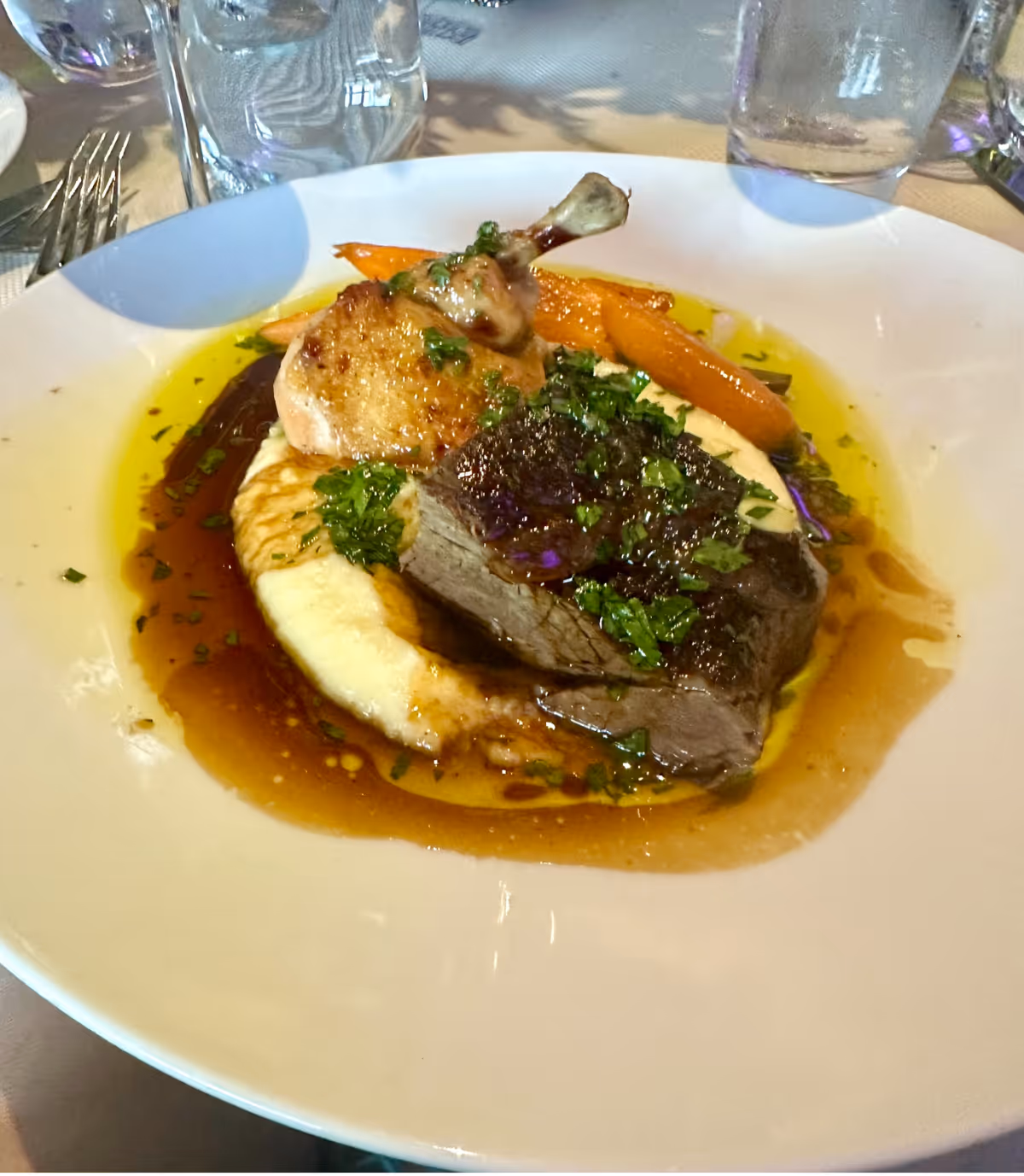 Plated entrée of beef and chicken served over mashed potatoes with carrots and a brown sauce on a white plate.