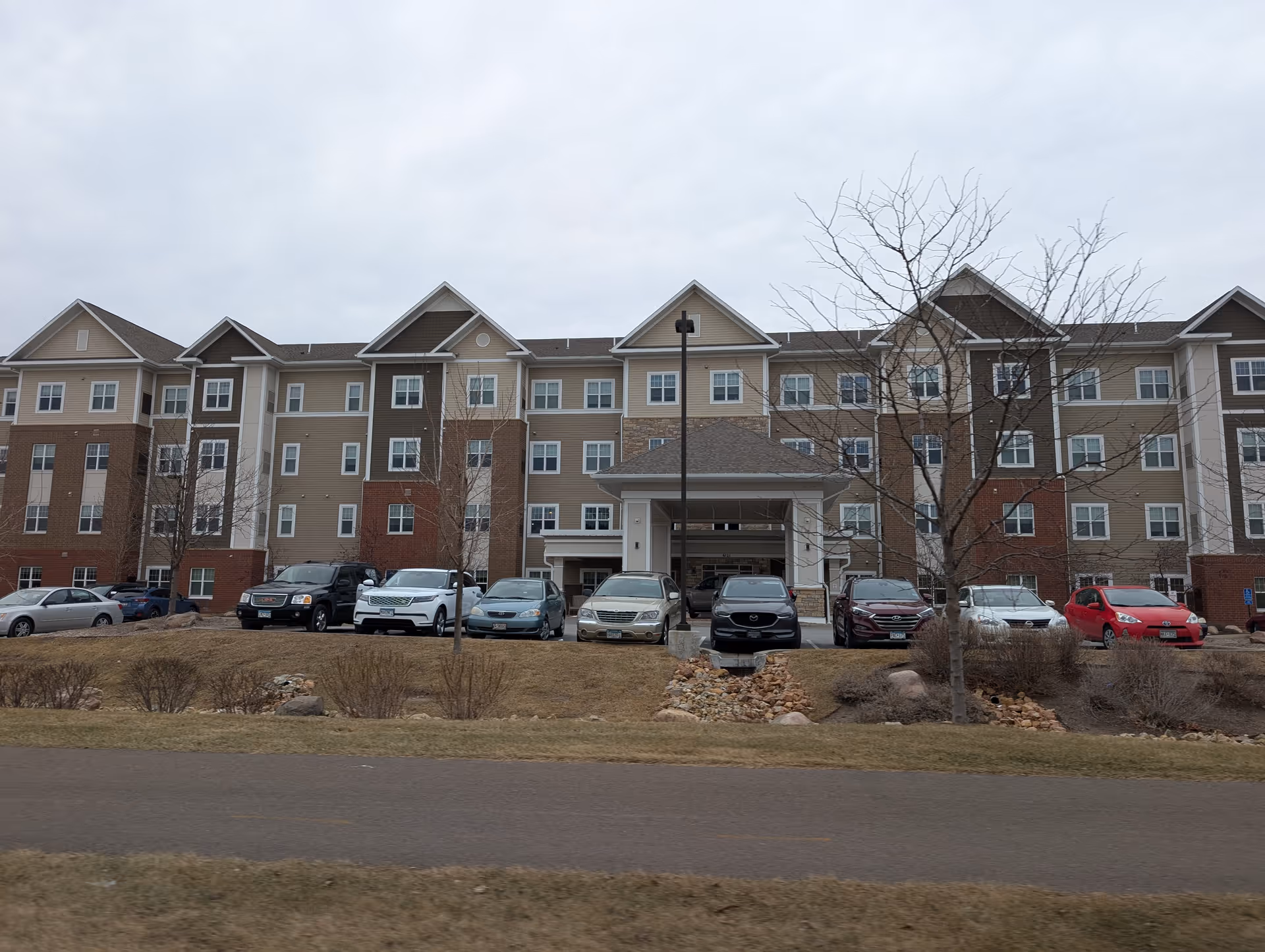 Front exterior of a multi-story senior living building with a covered entrance and cars parked in front.