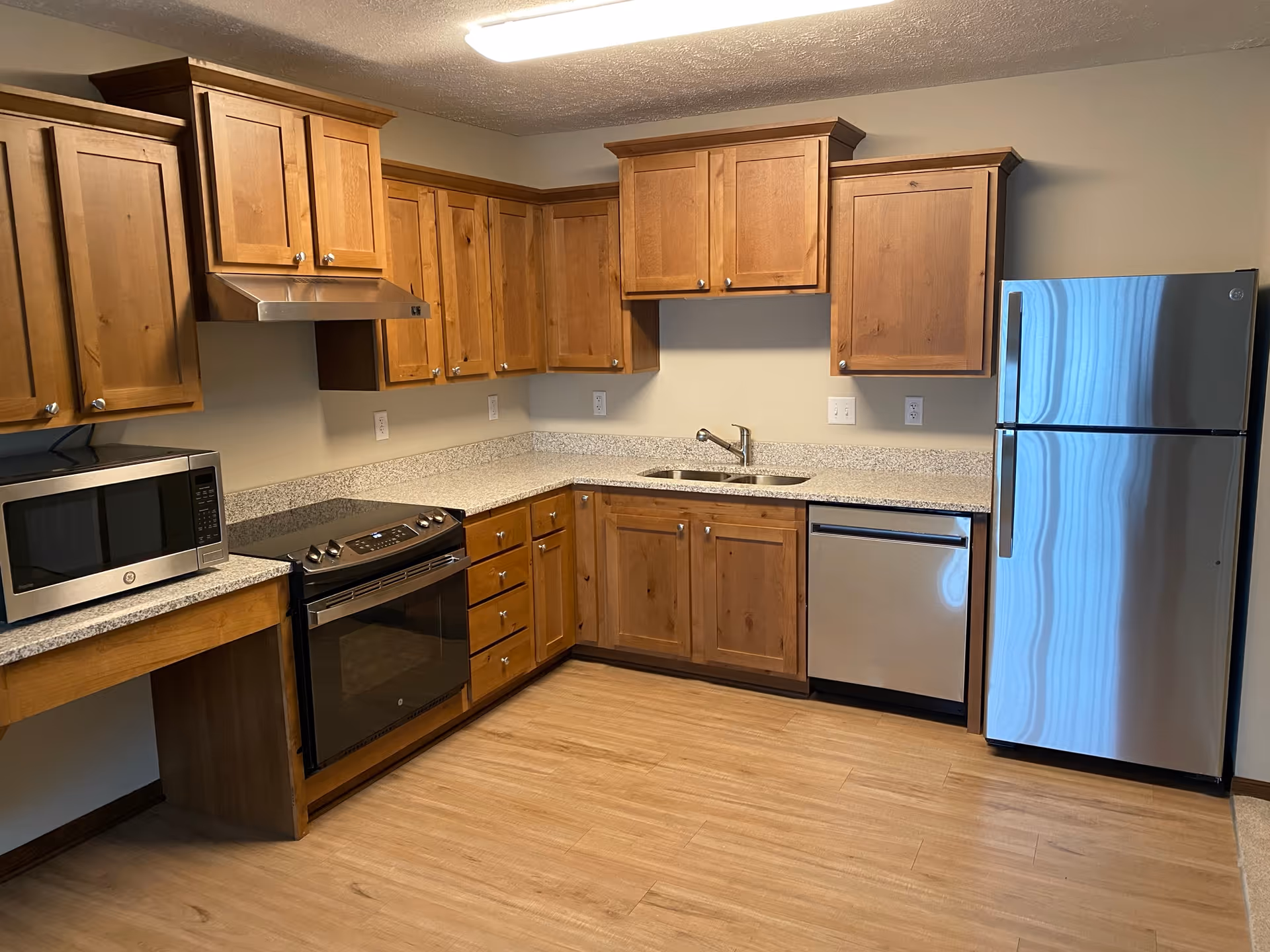 Clean kitchen with wooden cabinets, granite-look countertops, a sink, and stainless steel refrigerator, oven, dishwasher and microwave.