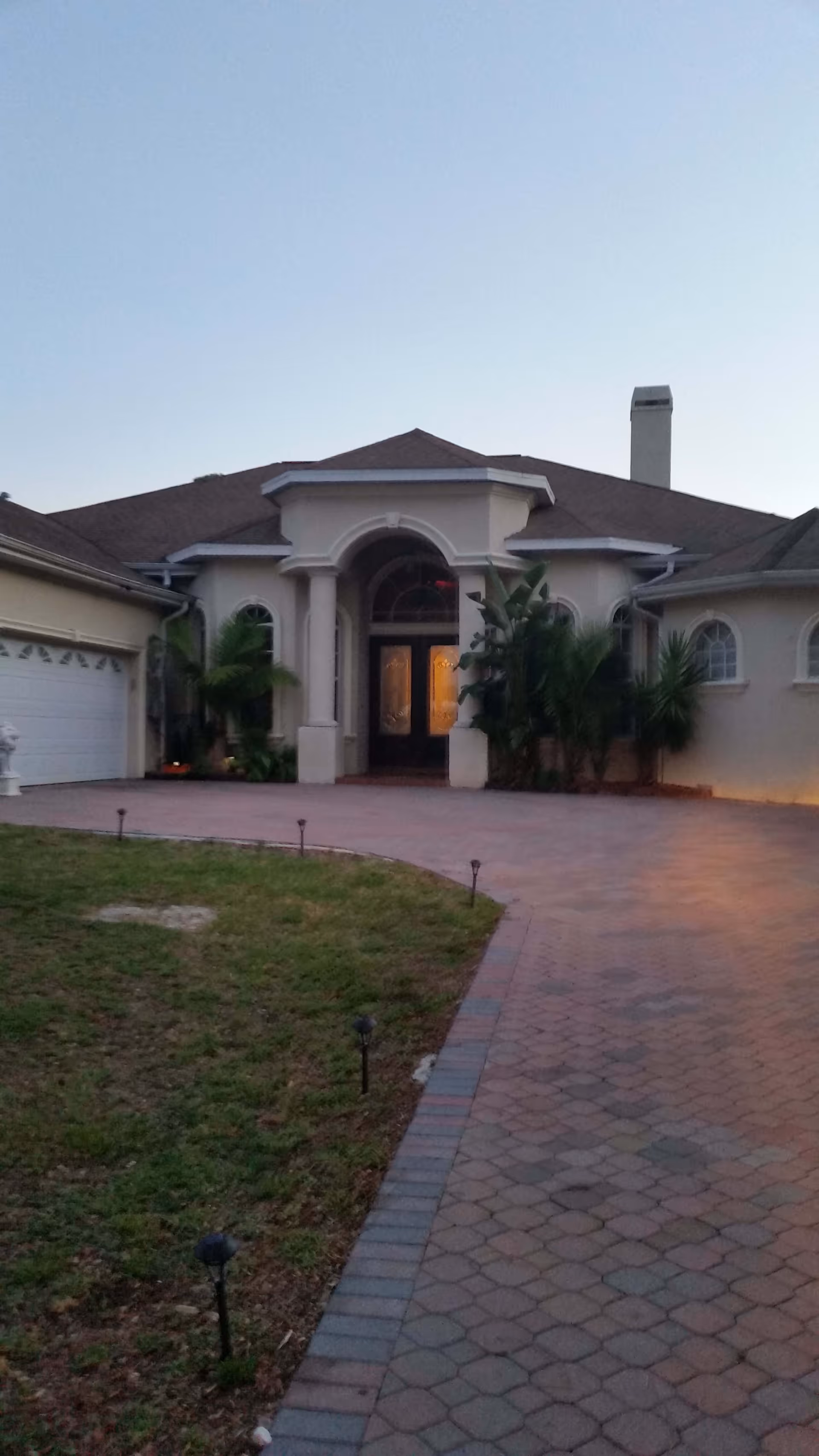 Front exterior of a large house with a paved driveway, columned arched entrance, and attached garage.
