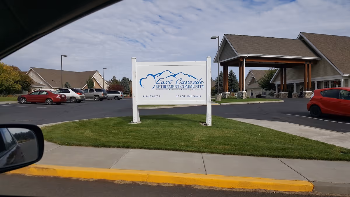 Entrance sign for East Cascade Retirement Community on a grassy median in front of the facility's covered entrance and parking lot.
