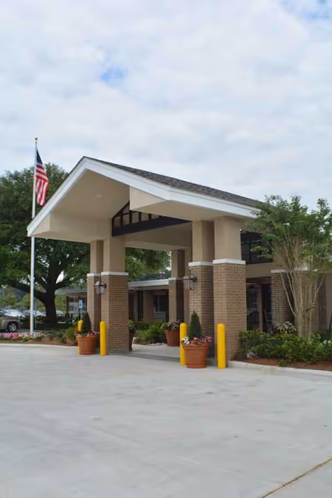 Exterior entrance of a senior living facility with brick columns and potted plants.