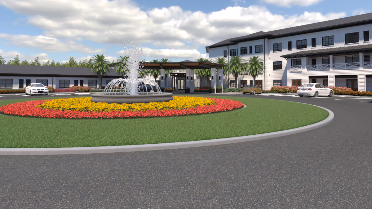 Front exterior view of Watercrest Santa Rosa Beach facility featuring a circular driveway with a central water fountain surrounded by colorful flower beds, palm trees, and a multi-story building with white siding and black roof under a partly cloudy sky.