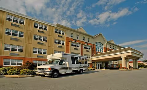 Ashbridge Manor exterior, a multi-story beige building with a white shuttle bus at the entrance canopy.