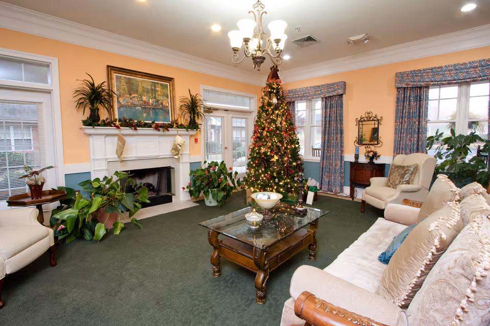 A festive living room with a decorated Christmas tree, fireplace, sofa, armchairs and a glass coffee table.