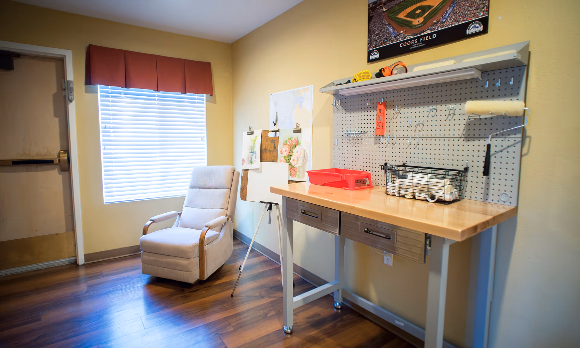 Well-lit interior activity room with a cushioned recliner by a window and a workbench with a pegboard and art supplies.