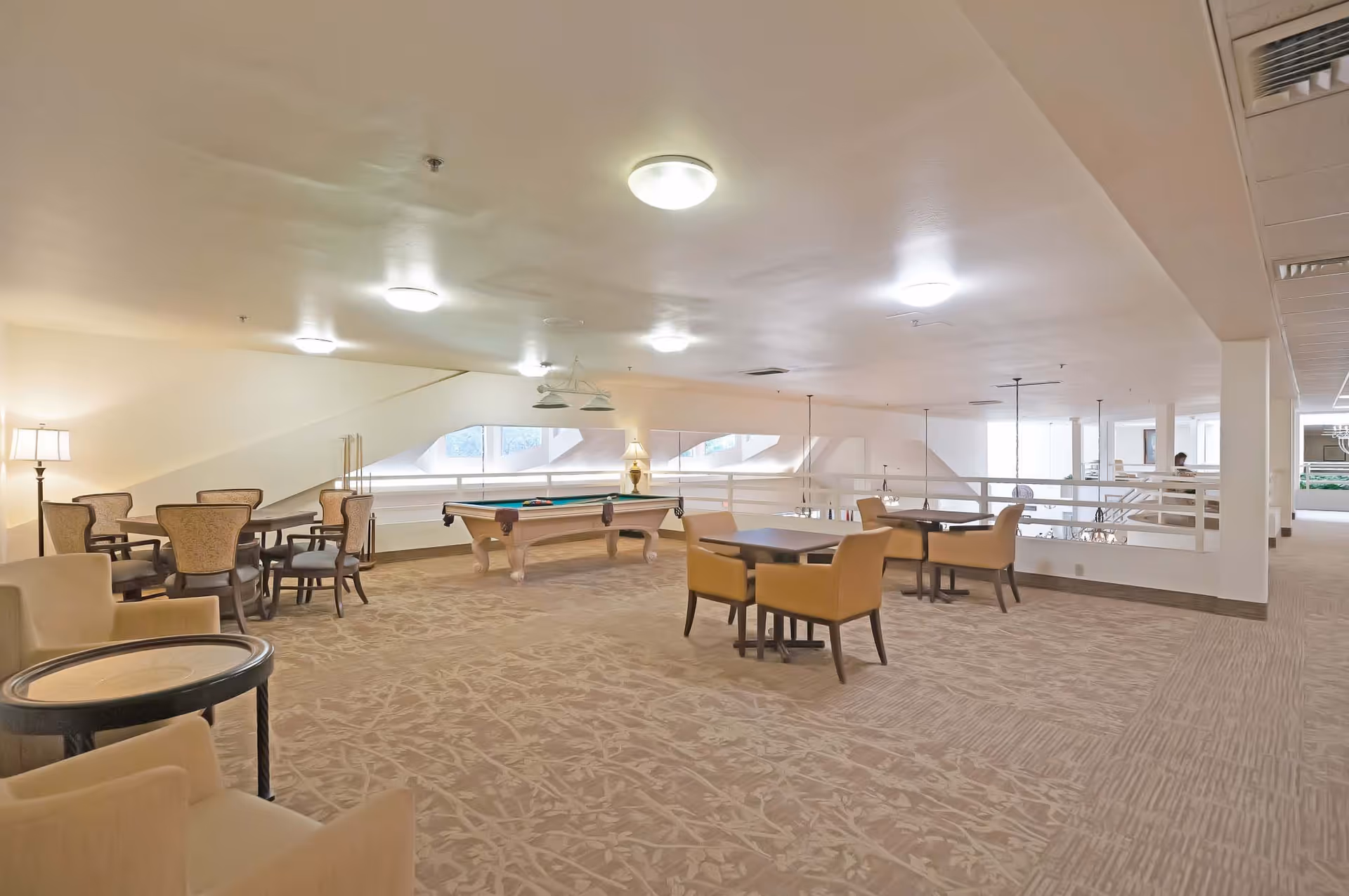 Spacious senior living common room with a pool table, multiple seating and dining tables, and soft overhead lighting.