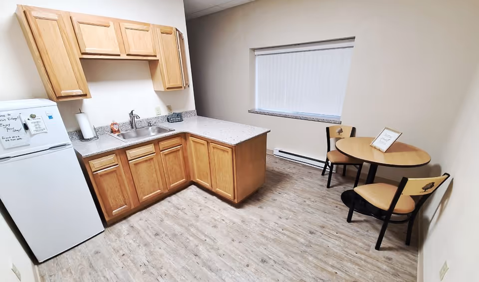 Small kitchenette with wooden cabinets, a sink, a mini refrigerator, and a round dining table with two chairs.