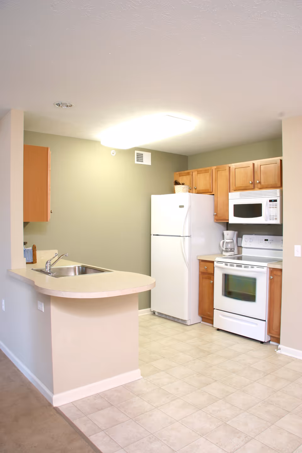 Small open kitchen with a curved countertop bar, stainless sink, white refrigerator, stove and microwave, and wooden cabinets.