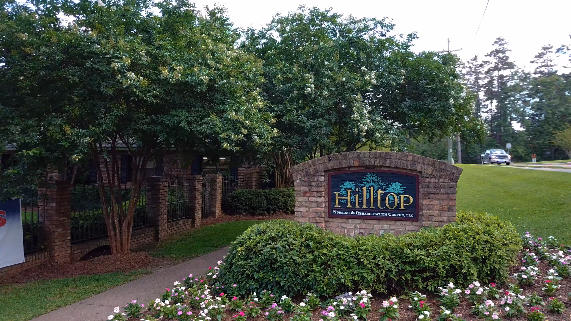 Brick monument sign for Hilltop Nursing & Rehabilitation Center, LLC at the facility entrance, surrounded by shrubs, flowers, and trees.