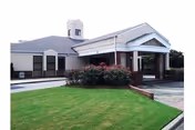 Exterior view of Wesley Gardens facility with lawn, shrubs, and a covered entrance.