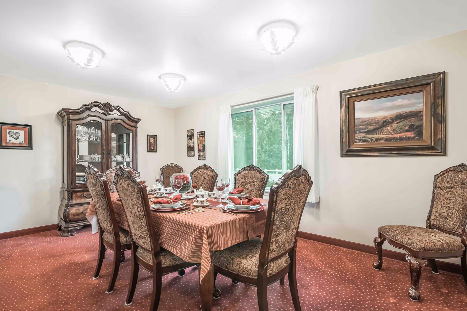 Formal dining room with a set table, upholstered chairs, a china cabinet, window, and framed artwork on the walls.