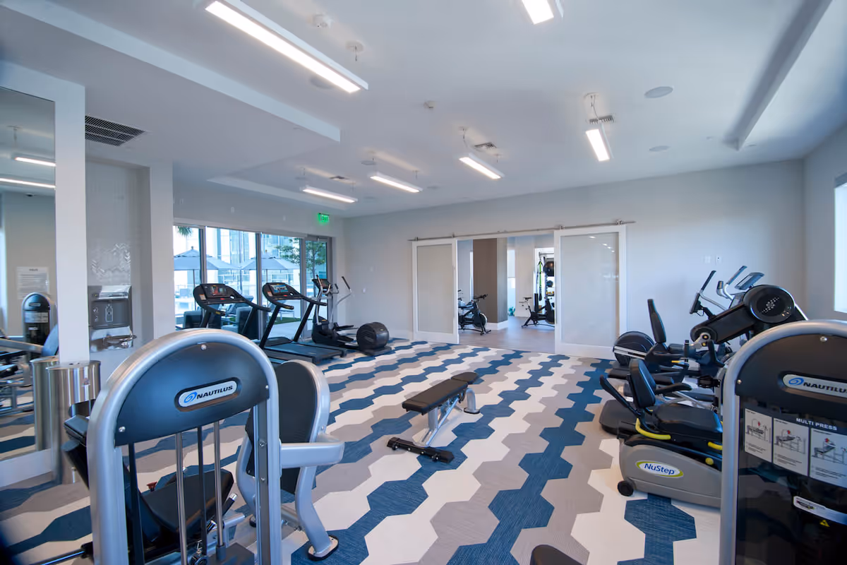 Bright fitness room with treadmills, weight machines, and a patterned blue-and-white floor.