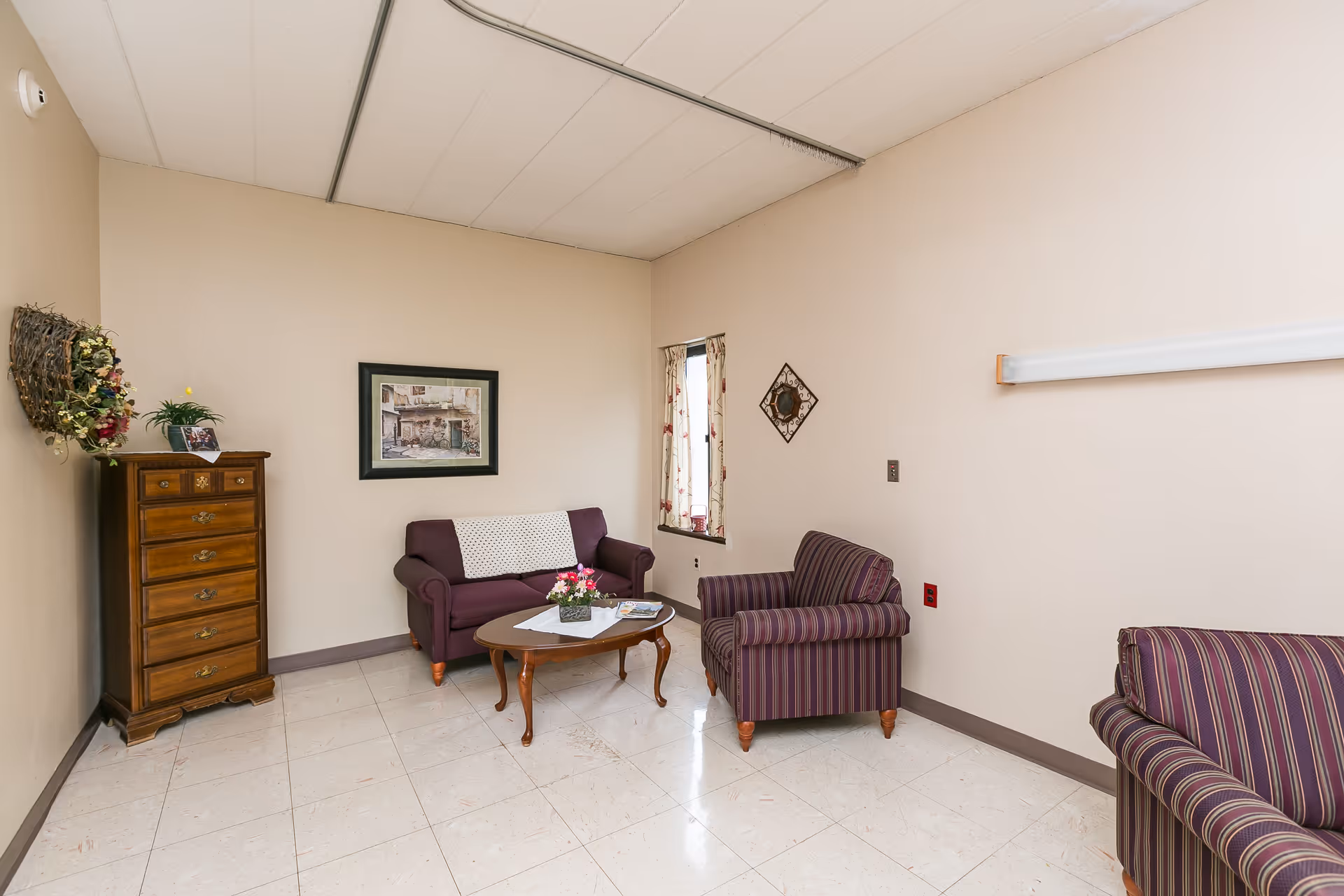 Small sitting room with a purple loveseat, two striped armchairs, a coffee table, a tall wooden chest, and framed wall decor.