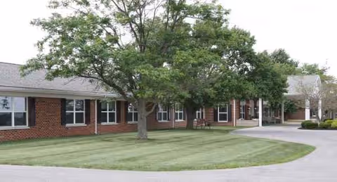 Red brick senior living facility exterior with green lawn, trees, and curved driveway.