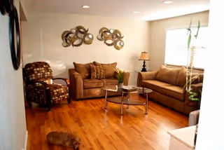Cozy living room with hardwood floors, two sofas, an armchair, a glass coffee table, wall art, and a window.