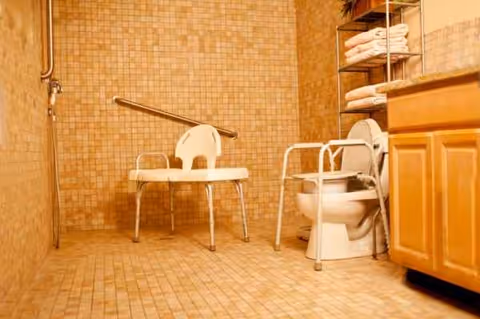Tile bathroom featuring a toilet, shower chair, grab bar, and wooden vanity.