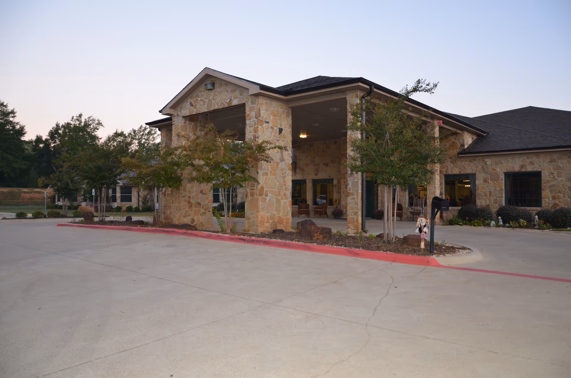 Exterior view of a stone building with a covered entrance and several small trees in front, part of a nursing and rehabilitation facility with a paved driveway and landscaped areas.