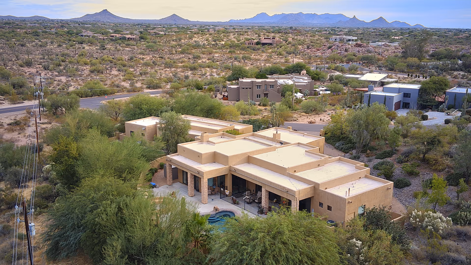 Aerial view of a single-story southwestern-style building with a patio and small pool surrounded by desert vegetation and distant mountains.