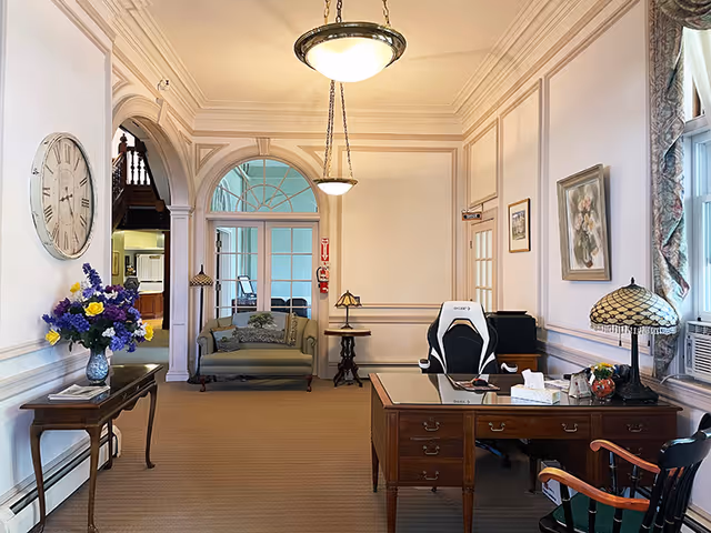 Bright traditional lobby with a wooden reception desk, seating area, decorative lamps, and floral arrangements.
