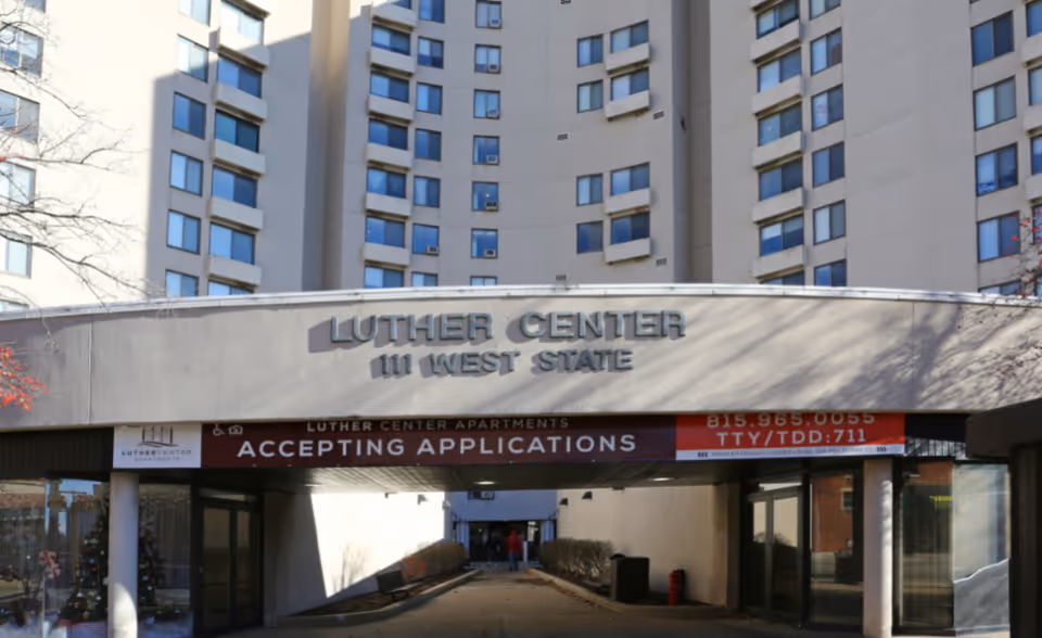 Front entrance of the Luther Center apartment building at 111 West State with a banner reading 'ACCEPTING APPLICATIONS'.