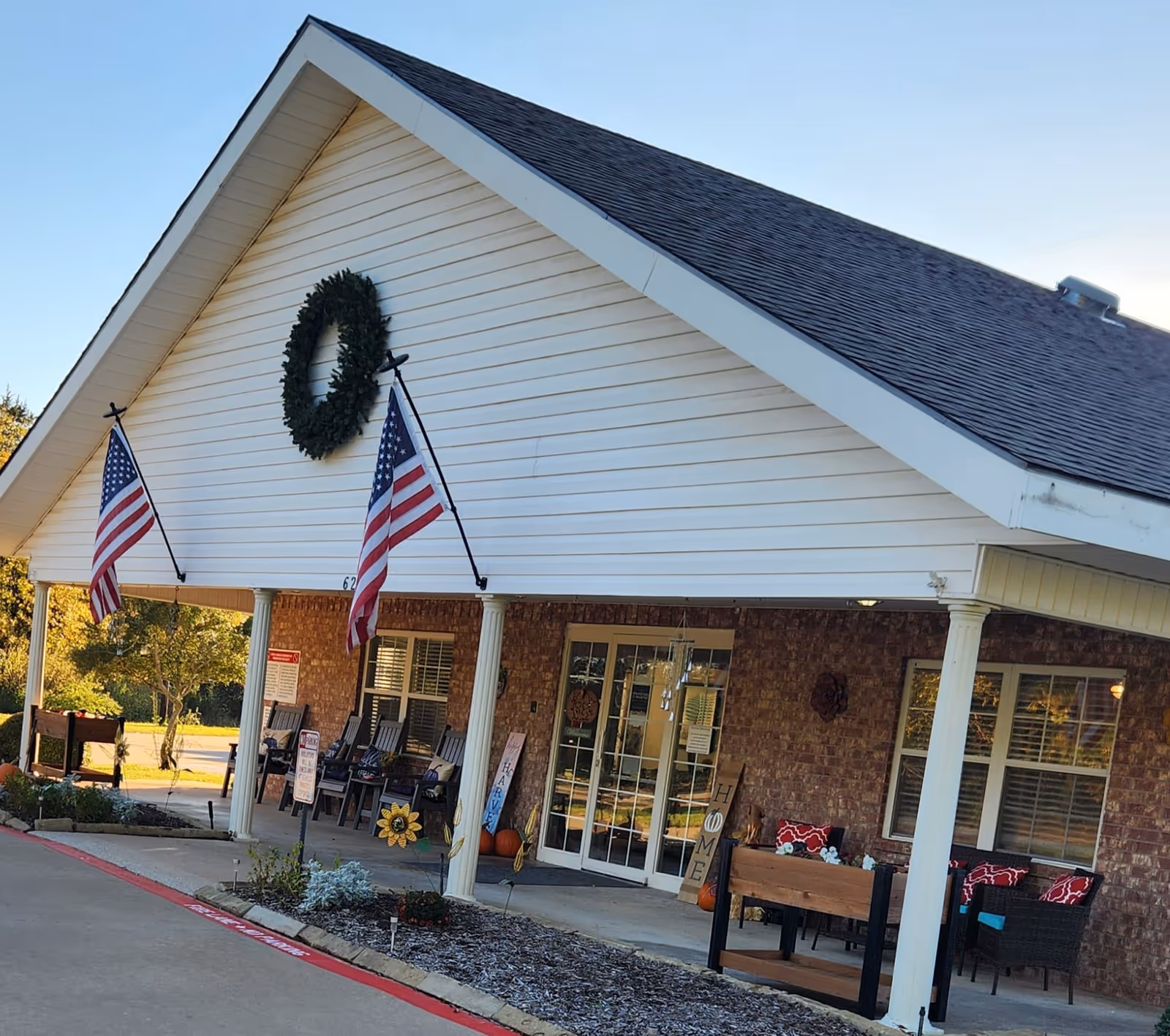 Front entrance of Preston Place with a covered porch, American flags, a wreath, seating, and decorative accents.