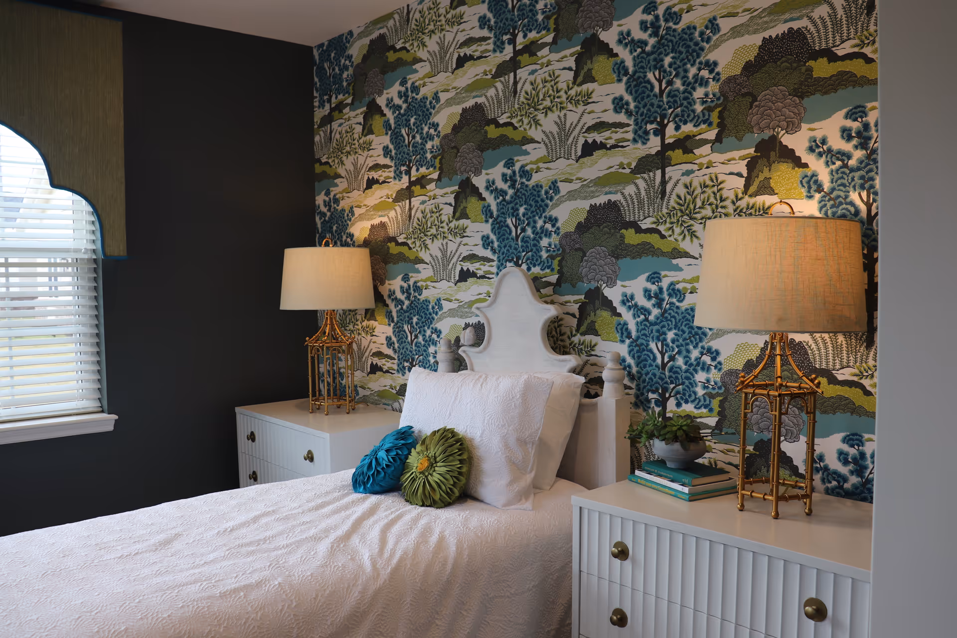 Single white bed in a bedroom with blue-green patterned wallpaper, matching nightstands and lamps.