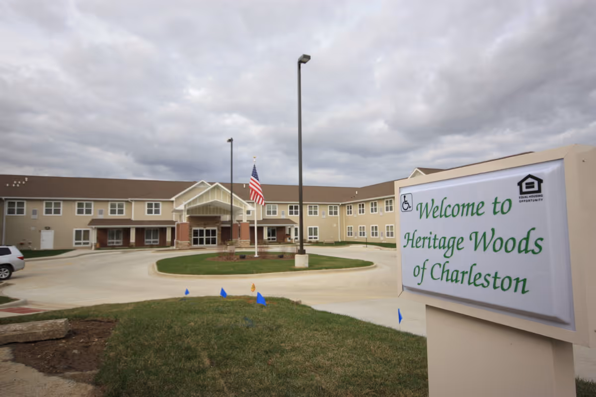 Exterior front view of the Heritage Woods of Charleston senior living building with a circular drive and a sign that reads "Welcome to Heritage Woods of Charleston".