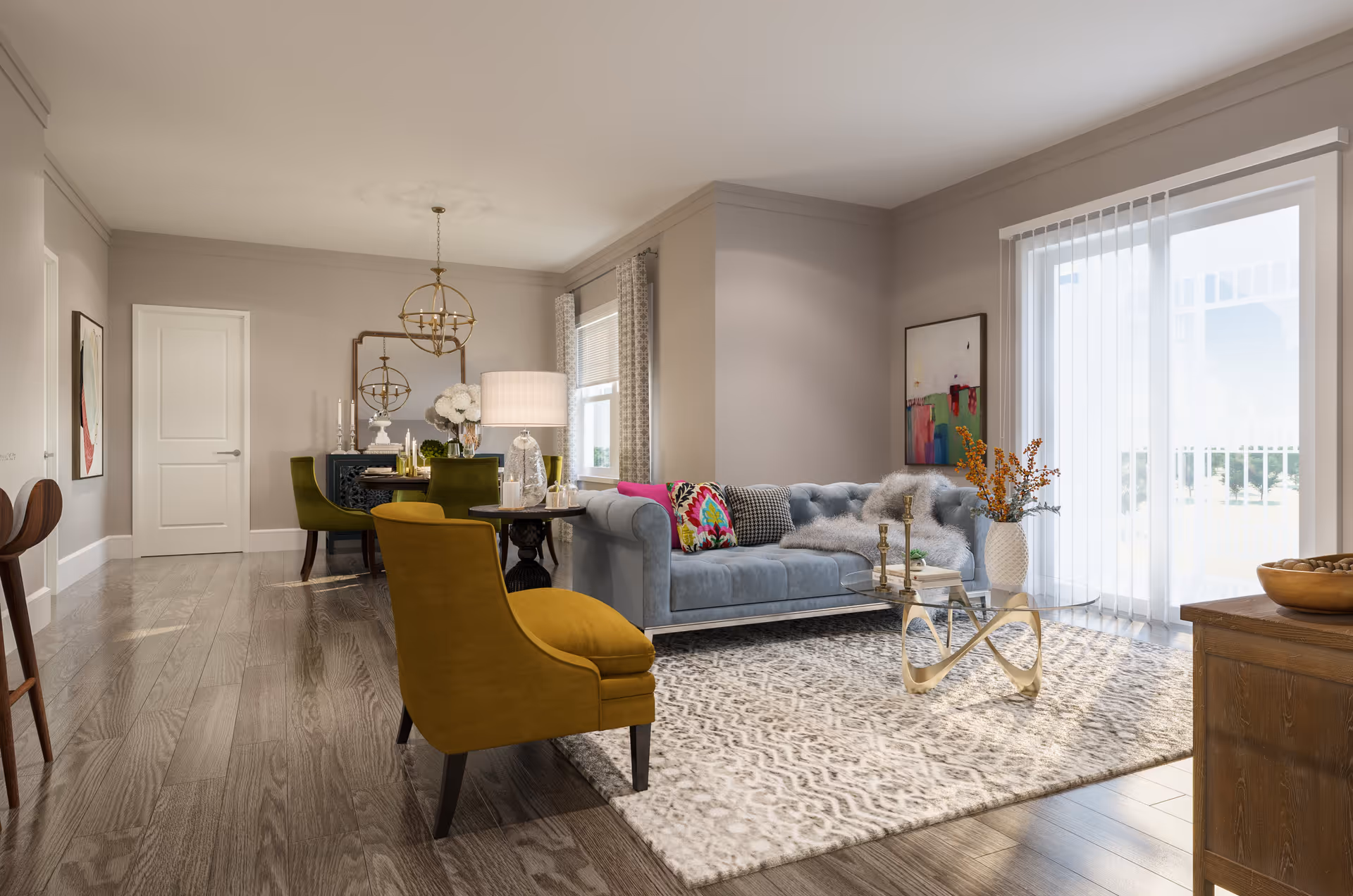 A bright and modern living room and dining area with wooden flooring. The living room features a light blue sofa adorned with colorful and patterned cushions, a glass coffee table with a decorative vase and flowers, and a mustard yellow armchair. Large sliding glass doors with vertical blinds allow natural light to fill the space. The dining area has a dark wooden table surrounded by green upholstered chairs, a decorative mirror, and a chandelier overhead. The walls are painted a soft beige, and there is artwork hanging on the walls.