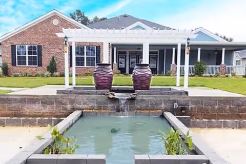 Front exterior of a brick-and-siding building with a pergola entrance and a tiered fountain pool in the foreground.