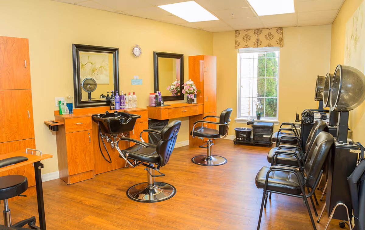 Bright salon room with styling chairs, mirrors, a shampoo sink and hooded hair dryers.