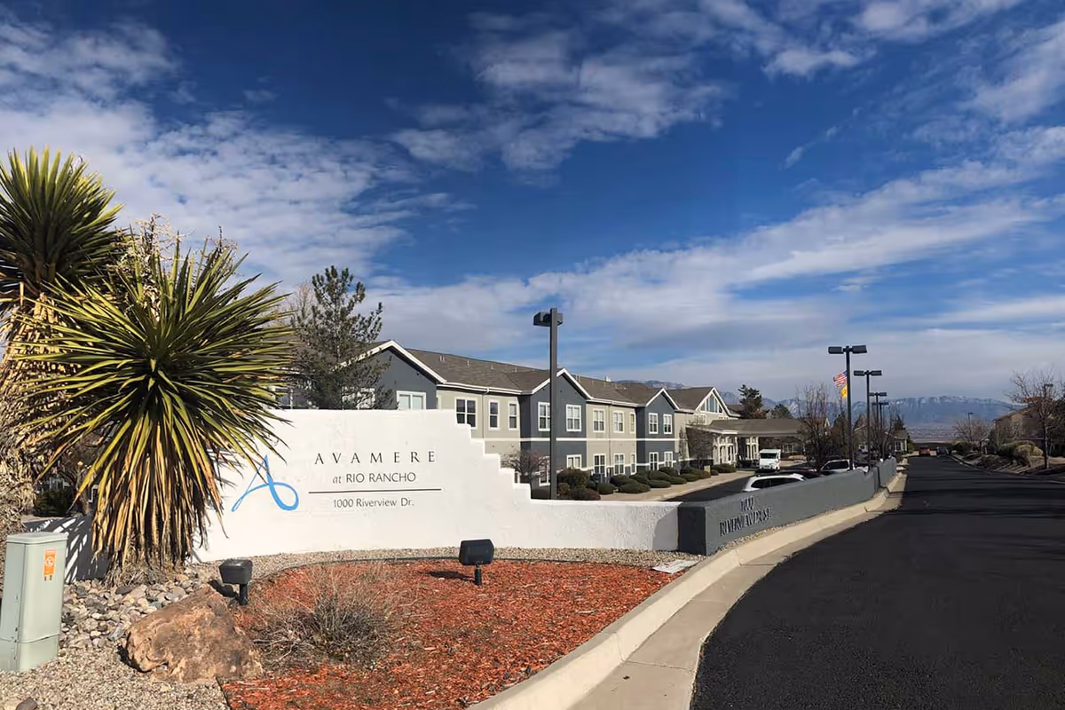 Entrance sign and front driveway of Avamere at Rio Rancho with the facility building, landscaping, and a blue sky.