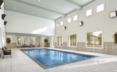 Bright indoor community swimming pool in a high-ceilinged room with windows and seating along the sides.