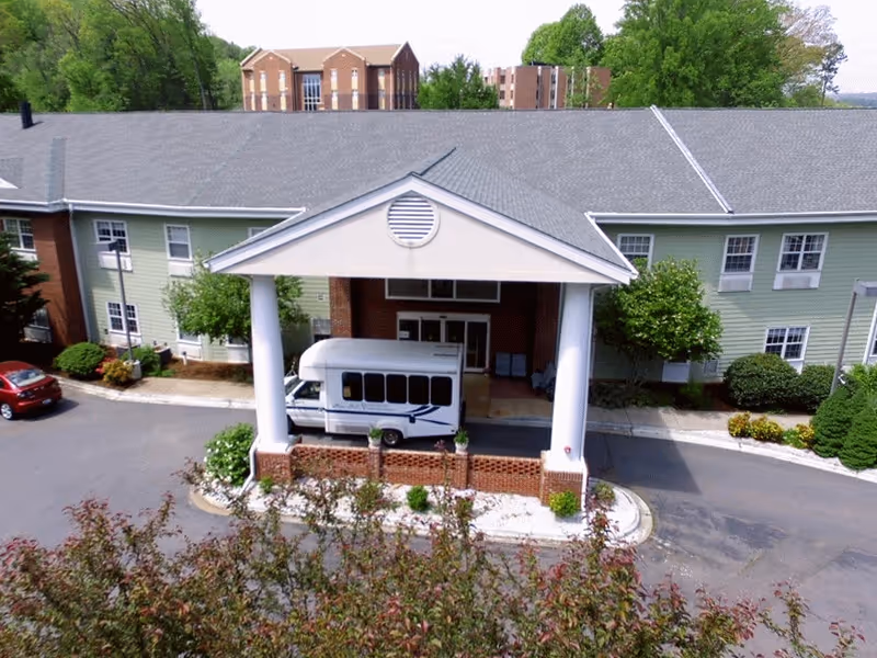 A senior living facility front entrance with a white bus under a porte-cochère.