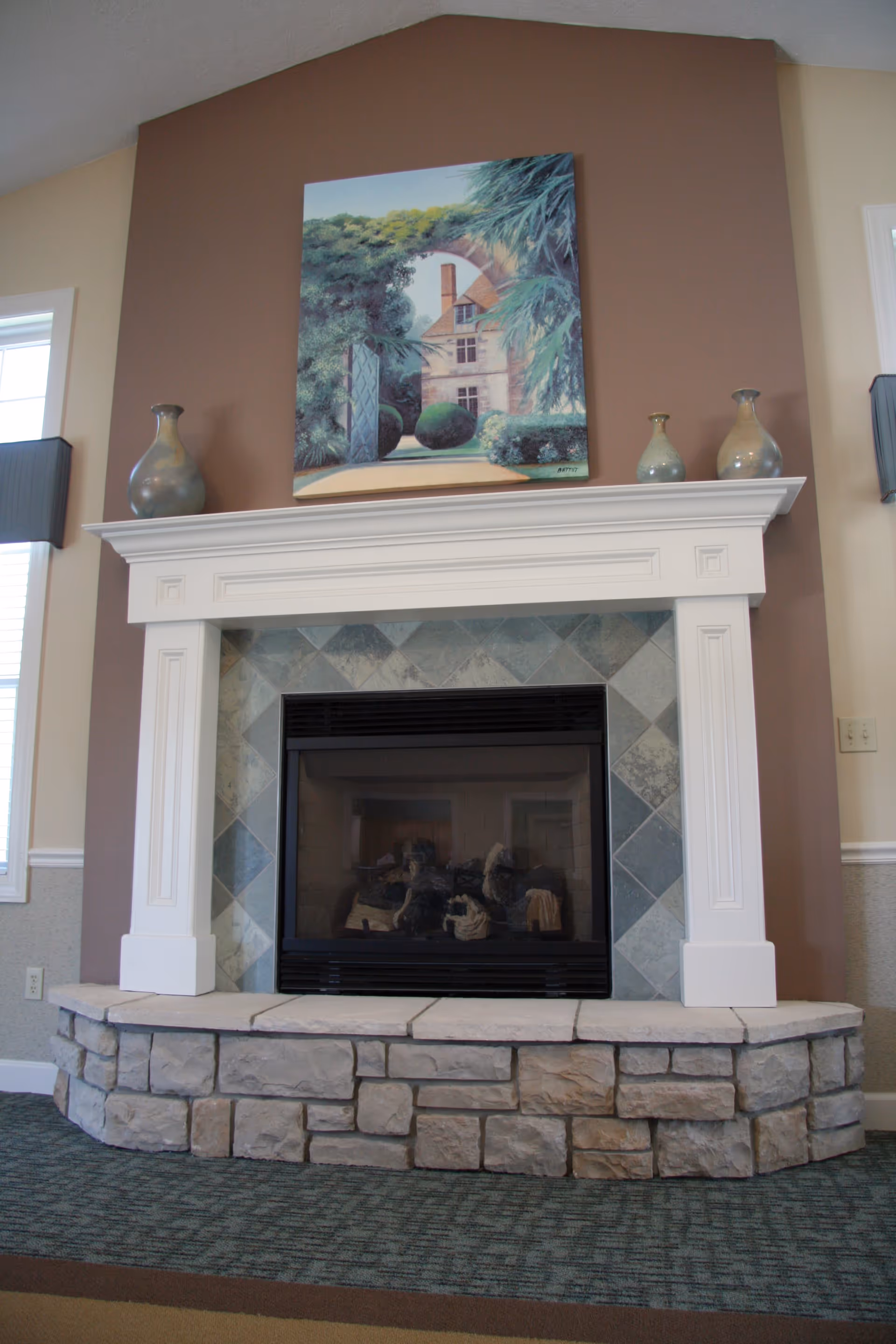 Stone hearth and white mantel fireplace with decorative vases and a painting mounted above.