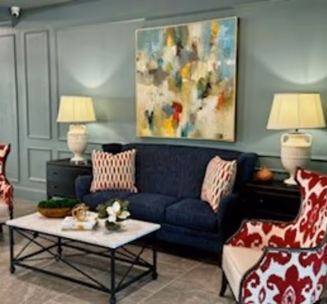A decorated sitting area with a navy sofa, patterned armchairs, a coffee table and an abstract painting on a paneled wall.