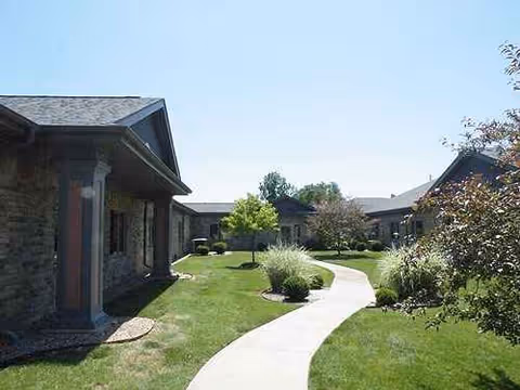 Curved walkway winds through a manicured outdoor courtyard beside stone buildings.