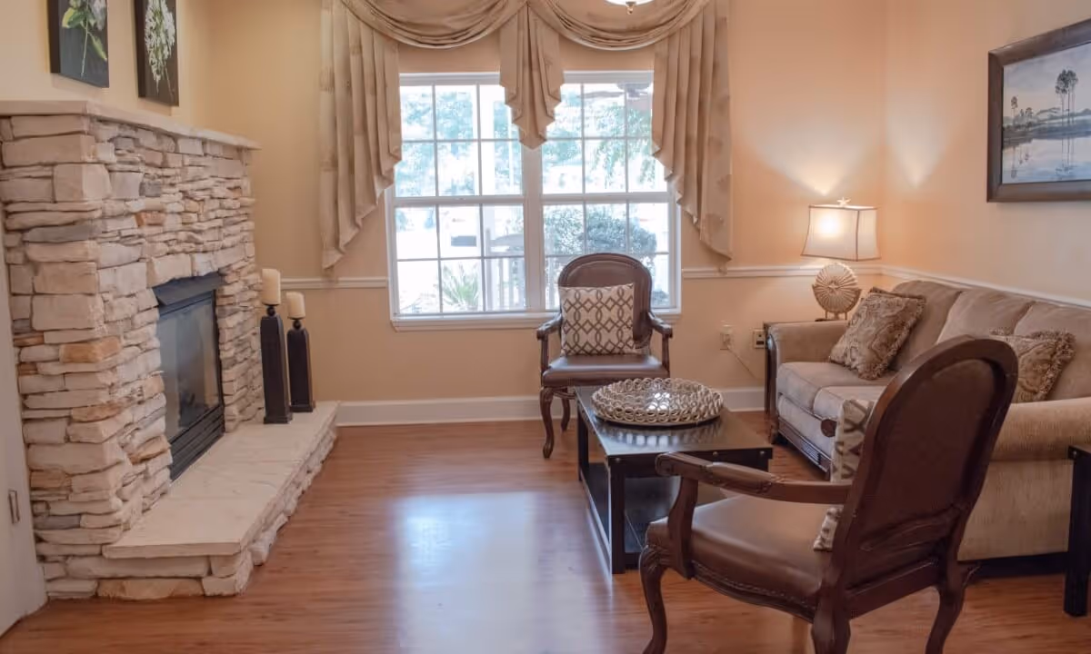 Cozy living room with a stone fireplace, sofa and armchairs arranged around a coffee table in front of a large window.