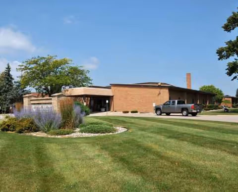 Brick senior living campus building with landscaped lawn and a parked pickup truck.