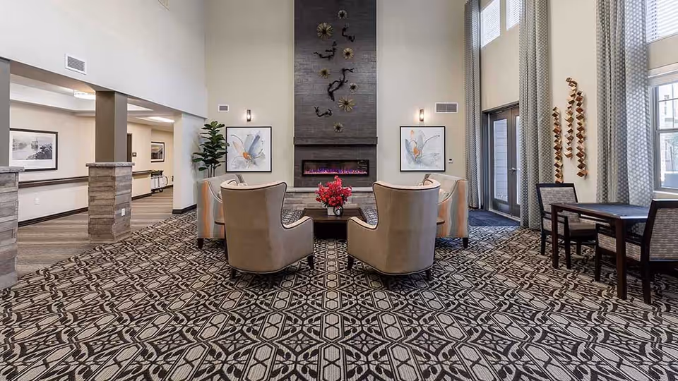 Lobby/lounge area with four armchairs around a coffee table facing a modern fireplace beneath a tall vaulted ceiling and large windows.