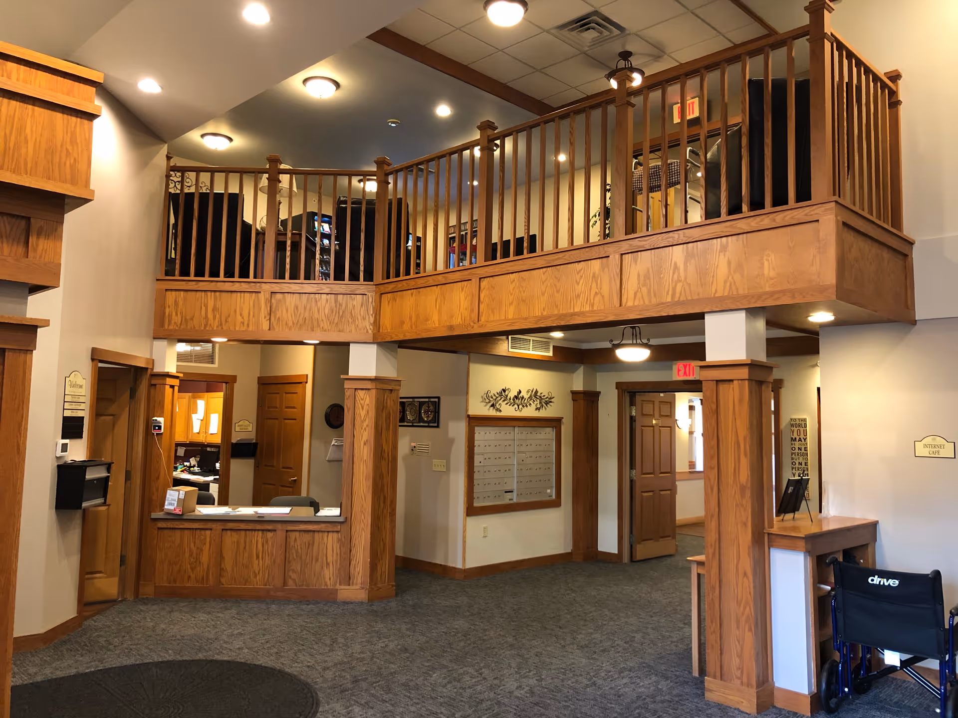 Lobby reception area with wood-paneled balcony, front desk, mailboxes and a wheelchair.