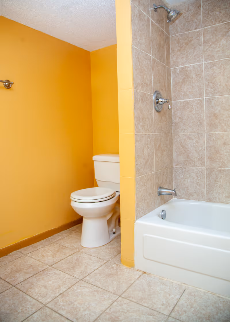 Bathroom with yellow walls featuring a white toilet and a bathtub with beige tiled walls and a showerhead.