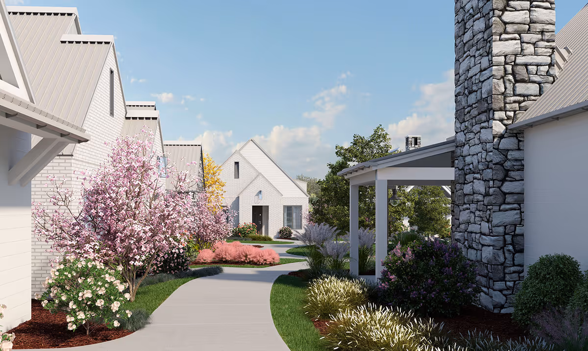 Curved walkway through a landscaped courtyard with flowering trees and white cottage-style buildings under a blue sky.