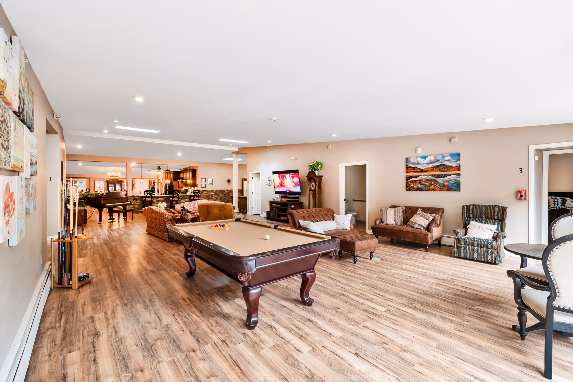 Spacious senior living common room with a pool table, seating areas, a television and a piano in the background.