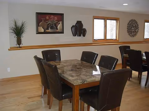 Dining room with a marble table, dark leather chairs, wall art, and windows.