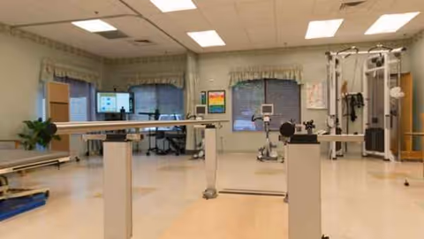 A spacious rehab room with parallel bars and various exercise machines.