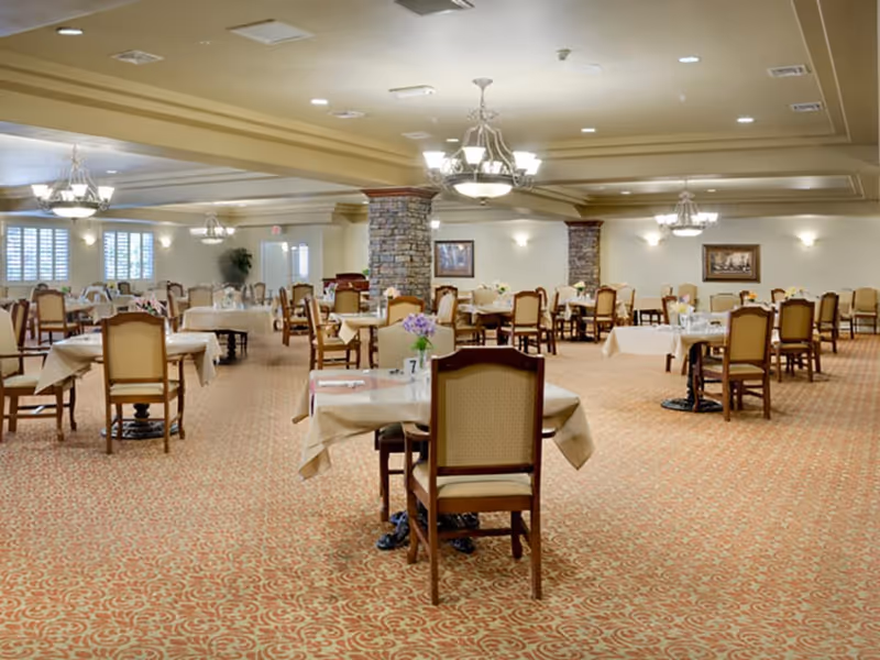 Spacious dining room with multiple set tables and chairs, chandeliers, and patterned carpet.