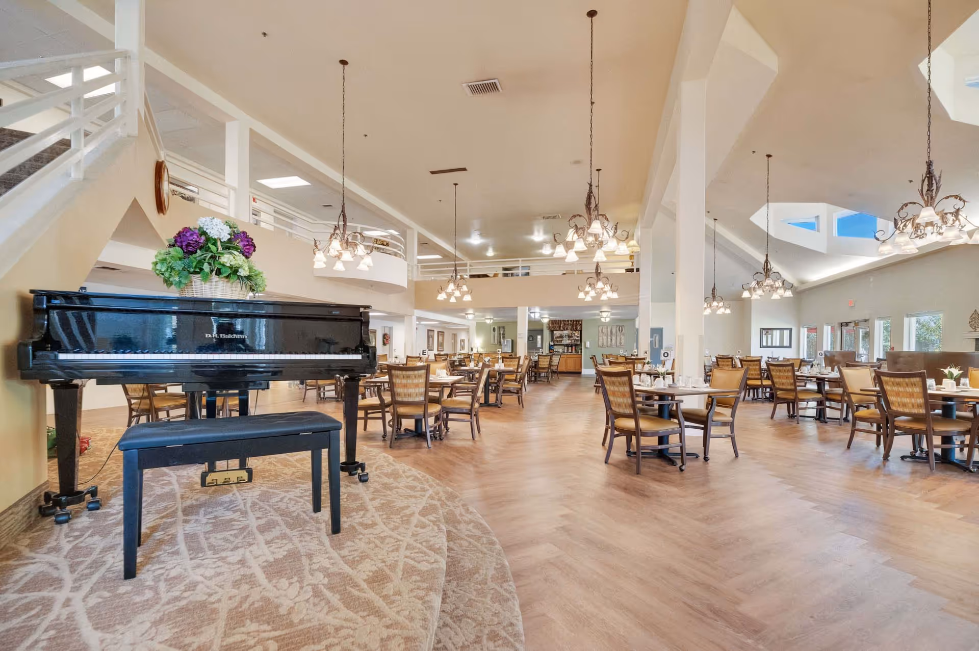 Spacious dining room with multiple tables and chandeliers and a black grand piano on a raised carpeted platform.