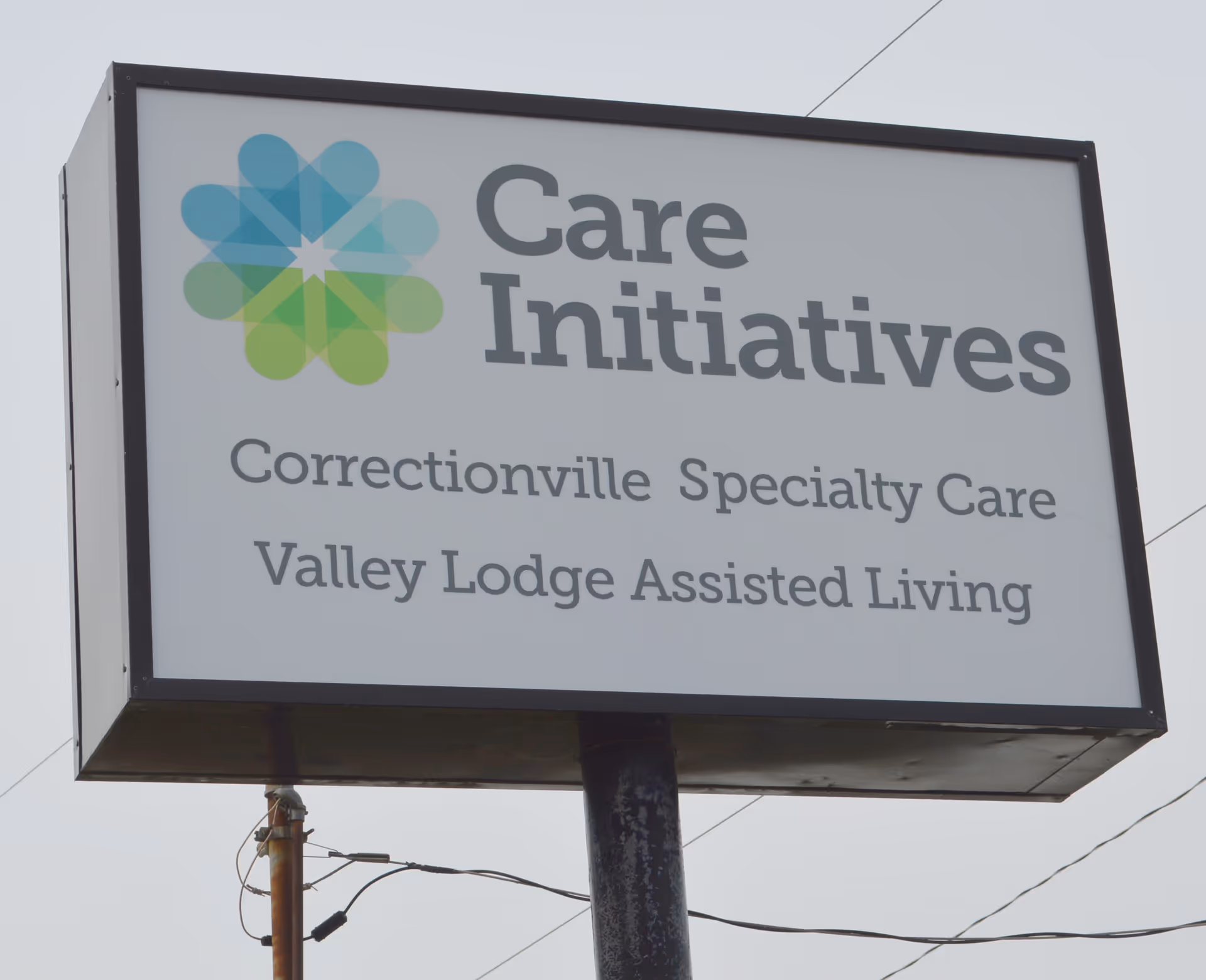 Outdoor sign for Care Initiatives, displaying the names Correctionville Specialty Care and Valley Lodge Assisted Living against a cloudy sky background.